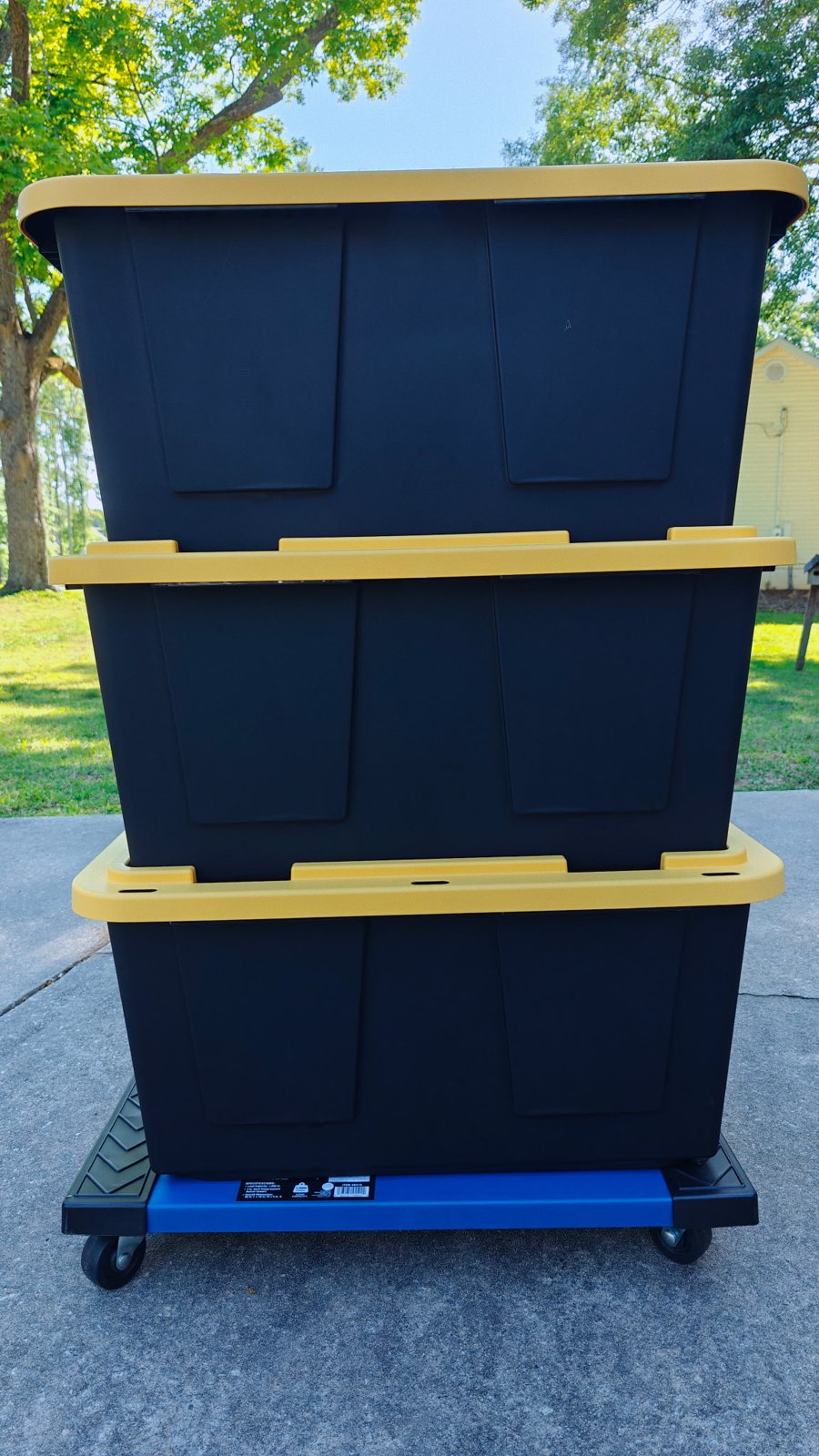 Three moving totes stacked on a rolling dolly in a driveway, ready for delivery